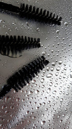 Brow lamination brushes on a wet, reflective surface.